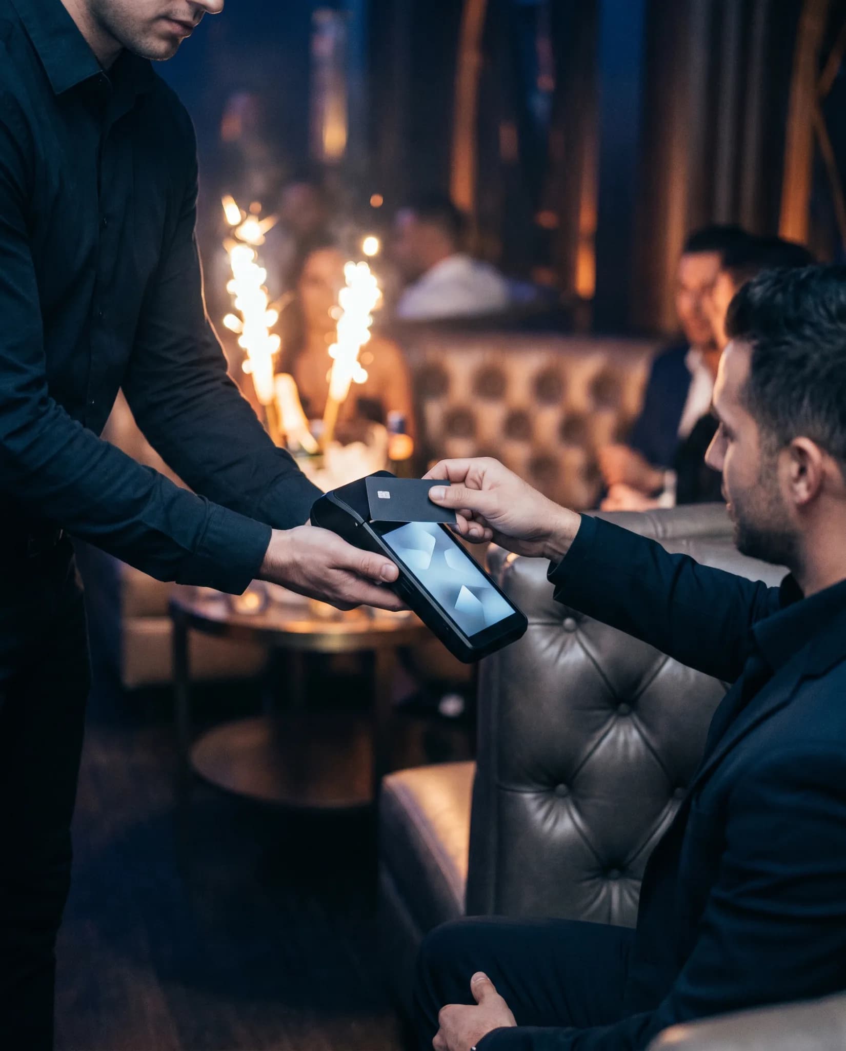 A guest tapping a card on a handheld terminal at a nightclub VIP table
